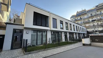 Moderne Reihenhäuser mit weißer Fassade, großen Fenstern und kleinen Vorgärten in städtischer Umgebung.