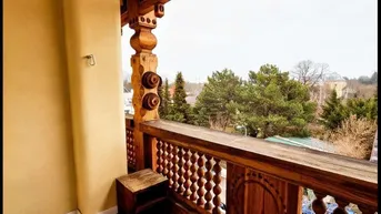 Traditioneller Balkon mit kunstvollem Holzgeländer und dunklem Holzboden, bietet einen Blick ins Grüne.