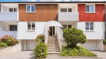 Mehrfamilienhaus mit farbigen Fassadenelementen, Balkonen und Garagen im Reihenhausstil.