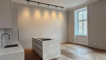 Moderne Küche mit Kochinsel, Fischgrätparkett und hohen Fenstern in einem hellen Raum.