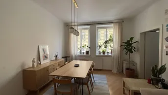 Heller Essbereich mit modernem Holztisch, Sideboard und Pflanzen am Fenster, offen zum Wohnbereich.