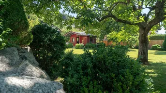 Idyllischer Gartenbereich mit gepflegtem Rasen, Bäumen und einem charmanten roten Gartenhaus im Hintergrund.