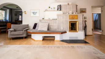 Gemütliches Wohnzimmer mit traditionellem Kachelofen, Holzboden und bequemen Sitzgelegenheiten.