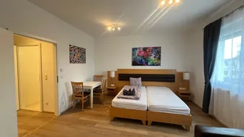 Helles Wohnzimmer mit Doppelbett, Esstisch und Holzboden, ideal für Gäste.
