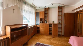 Helles Wohnzimmer mit Fischgrätparkett, Holzmöbeln und einem großen Fenster mit Vorhängen.