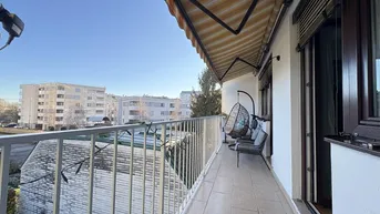 Geräumiger Balkon mit Markise, Sitzgelegenheiten und Blick auf die umliegenden Gebäude.