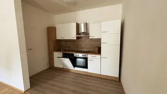 Kleine, moderne Einbauküche mit weißen Schränken und Holzoptik-Arbeitsplatte.