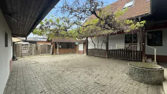 Gepflasterter Innenhof mit Baumbestand und Zugang zu Nebengebäuden unter blauem Himmel.
