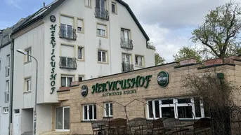 Gebäudeansicht des Hervicushofs mit Restaurantbereich und Außenbestuhlung unter einem mansardförmigen Dach.