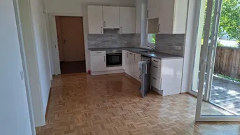 Heller Wohn- und Essbereich mit integrierter Küche, Parkettboden und Zugang zum Balkon.