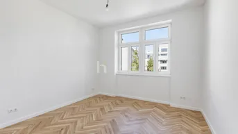 Helles, leeres Zimmer mit Fischgrätparkett und großem Fenster, bereit zum Einzug.