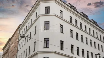 Weißes Eckgebäude mit vielen Fenstern und moderner Architektur unter einem dramatischen Himmel.