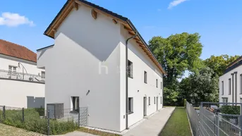 Seitenansicht eines modernen Neubaus mit weißer Fassade und gepflegtem Außenbereich unter blauem Himmel.