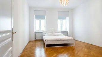 Helles Schlafzimmer mit Fischgrätparkett, weißen Wänden und zwei großen Fenstern.