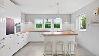 Helle, moderne Küche mit weißen Schränken, Holz-Arbeitsplatten und einer Kücheninsel mit Barhockern.