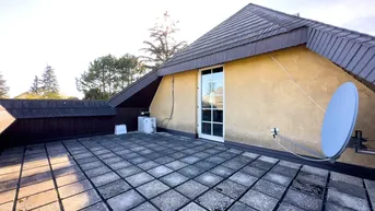 Große Dachterrasse mit Fliesenboden und Blick auf die Umgebung unter blauem Himmel.