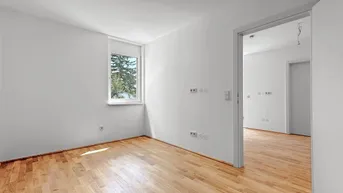 Helles Schlafzimmer mit Parkettboden und Fenster, das einen grünen Ausblick bietet.