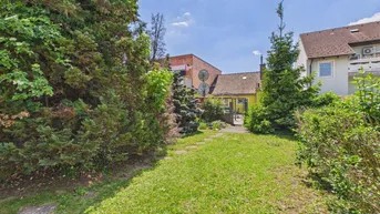 Grüner Gartenbereich mit Rasenfläche und Bäumen, der zum Haus im Hintergrund führt.