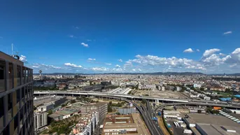 Weitläufiger Blick über die Stadt mit Autobahnkreuz und urbaner Bebauung unter blauem Himmel.