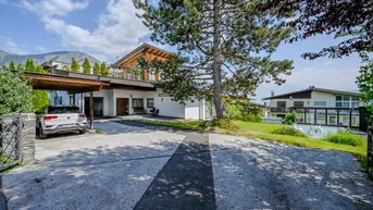 Einfamilienhaus mit Carport, Auffahrt und Bergblick unter blauem Himmel.
