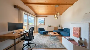 Helles Wohnzimmer mit Holzbalkendecke, Arbeitsbereich und Panoramablick auf die Berge.