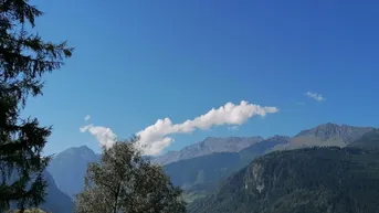 Malerischer Bergblick unter blauem Himmel mit einigen Wolken und Bäumen im Vordergrund.