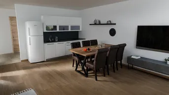 Heller offener Wohn-Essbereich mit integrierter Küche, Holzboden und modernem Esstisch.