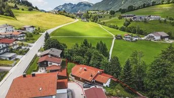 Luftaufnahme eines Hauses mit roter Grundstücksgrenze in einer grünen, bergigen Landschaft.