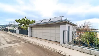 Moderne Garage mit Sektionaltor und Photovoltaikanlage auf dem Dach, an einer Wohnstraße gelegen.