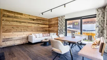 Geräumiger Wohn-Essbereich mit Holzwand, bequemer Sitzecke und Zugang zum Balkon.
