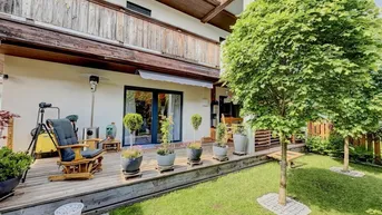 Geräumige Holzterrasse mit Gartenmöbeln, umgeben von einem gepflegten Rasen und Bäumen.