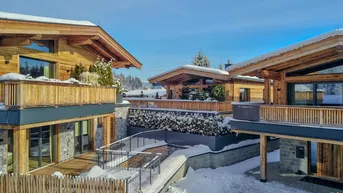 Moderne Chalets mit Holzfassaden und schneebedeckten Dächern in alpiner Umgebung.