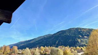 Panoramablick auf die umliegenden Berge und herbstliche Natur von einem Balkon aus.