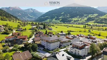 Panoramablick auf eine Siedlung in einem grünen Tal, umgeben von majestätischen Bergen.
