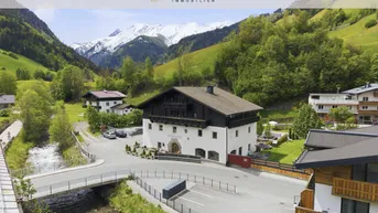 Traditionelles Gebäude in einem malerischen Tal mit schneebedeckten Bergen und üppiger grüner Landschaft.