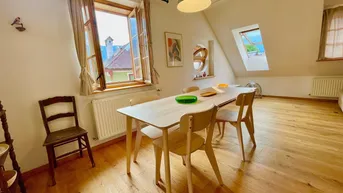 Helles Esszimmer im Dachgeschoss mit Holzboden, modernem Esstisch und Blick auf die Umgebung.