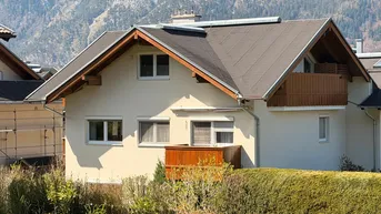 Charmantes Haus mit Holzbalkonen und Bergblick, umgeben von grüner Landschaft.