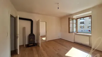 Helles Wohnzimmer mit Holzboden, einem modernen Holzofen und Blick auf die umliegenden Gebäude.