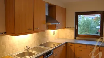 Funktionale Küche mit Holzschränken, integriertem Kochfeld und Blick ins Grüne durch das Fenster.