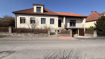 Vorderansicht des Hauses mit Satteldach, Balkon und gepflegtem Vorgartenbereich.