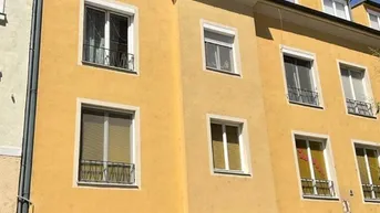 Gelbe Fassade eines Mehrfamilienhauses mit Ladenlokal im Erdgeschoss und mehreren Fenstern.