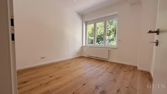 Helles Schlafzimmer mit Blick ins Grüne, ausgestattet mit neuem Holzparkettboden und großen Fenstern.