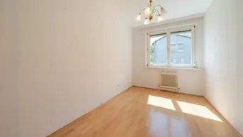 Sonniger Raum mit Parkettboden und Fenster, das einen Blick auf ein Gebäude bietet.