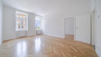 Helles Zimmer mit Fischgrätparkett, weißen Wänden und zwei großen Fenstern.
