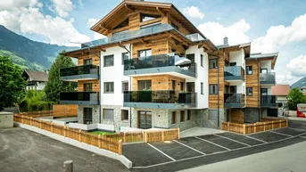 Modernes Mehrfamilienhaus in alpiner Architektur mit Holzfassade, Balkonen und Parkplätzen im Freien.