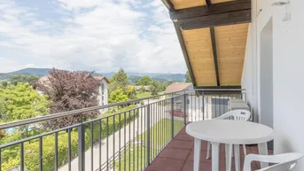 Balkon mit Gartenmöbeln und einem weiten Blick über die grüne Landschaft und umliegende Häuser.