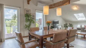 Heller Essbereich mit Holztisch, Ledersesseln, freiliegenden Holzbalken und Zugang zum Balkon mit grüner Aussicht.