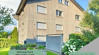 Modernes Mehrfamilienhaus mit Holzfassade und gepflegtem Gartenbereich, umgeben von grüner Natur.