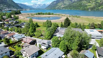 Panoramablick auf die Wohnsiedlung mit dem Zeller See und den umliegenden Bergen unter blauem Himmel.