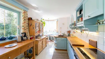 Helle Küche im Landhausstil mit hellblauen Schränken, Holztheken und einem Essbereich am Fenster.